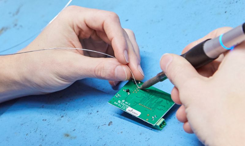 Close-up of an engineer soldering wires onto a printed circuit board as part of an early hardware prototype.