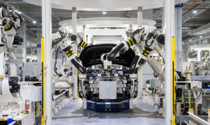 Industrial robots assembling a vehicle on an automated production line inside a modern factory, illustrating smart manufacturing and connected industrial systems.